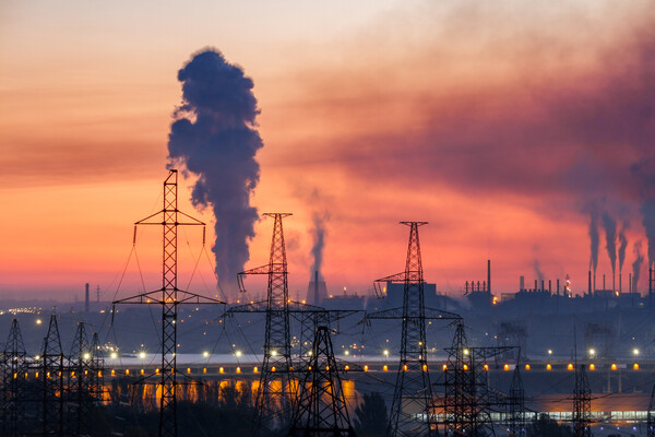 Industrial landscape with electric power lines, hydroelectric dam and metallurgical plants with smoke in the sky.