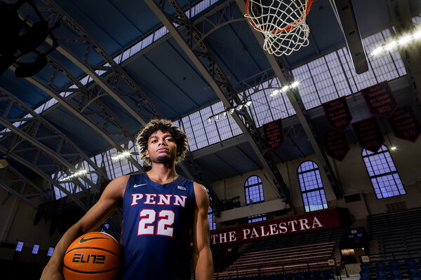 Lucas Monroe stands under the hoop at the Palestra holding a basketball at his side.