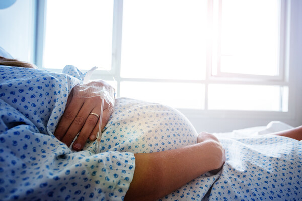 Pregnant person laying in a bed with an IV drip in their arm.