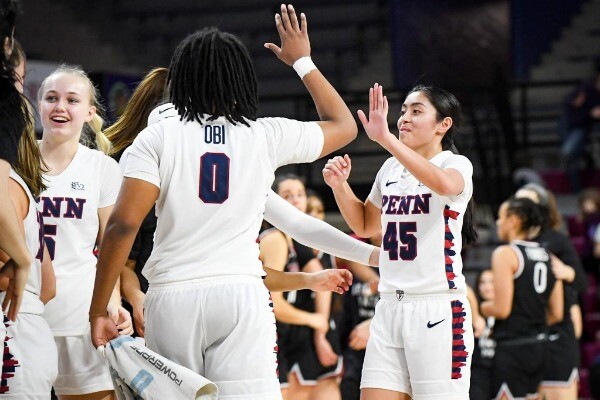 Wearing their white Penn jerseys, Jordan Obi, left, and Kayla Padilla, right, high five during a game along the sidelines.