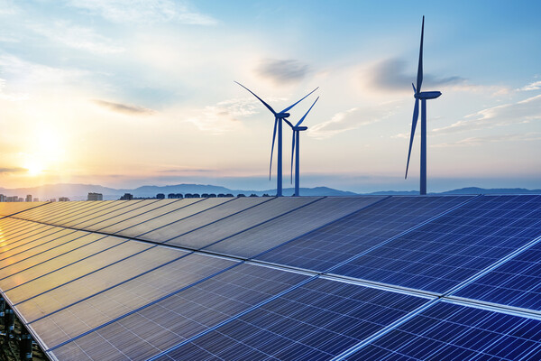 Solar panels and three wind turbines set against a blue sky and setting sun. 