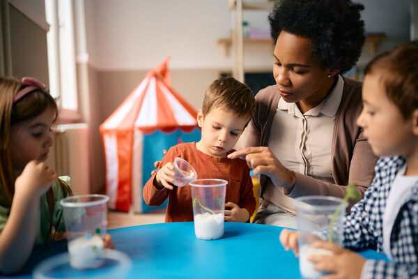 A childcare worker at a table with three young children.