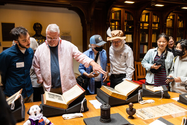 About six people standing looking at open books on a table in a library