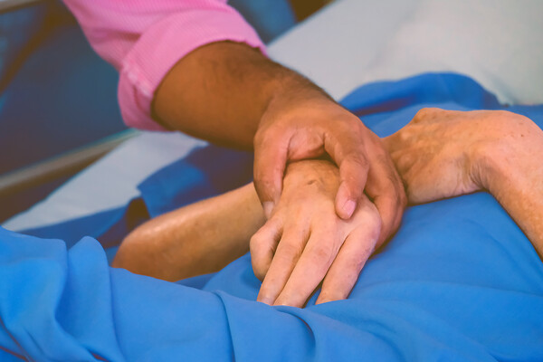 A hand holding a dying person’s hand in a hospital bed.