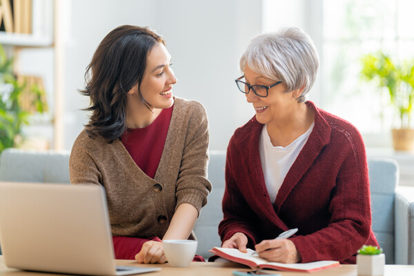 Two people gathered around a laptop with a notebook and pen