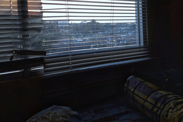 View of a city out of broken blinds from a bedroom.