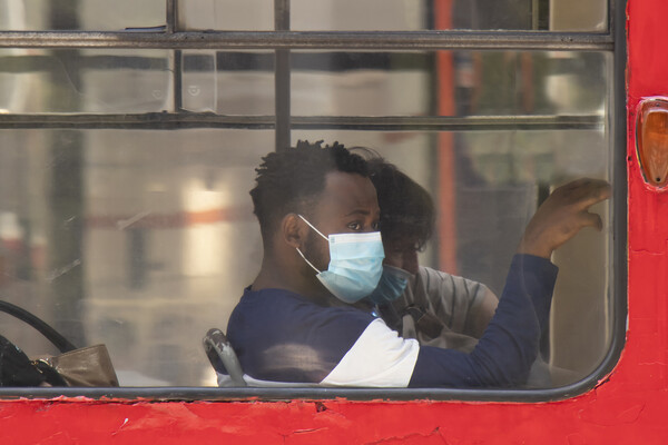 Young black man wearing surgical face masks while sitting and riding on a window seat of a tram