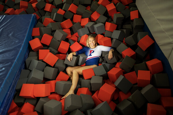 Wearing her Penn leotard, McCaleigh Marr lies in a pile of foam blocks, next to a mat.