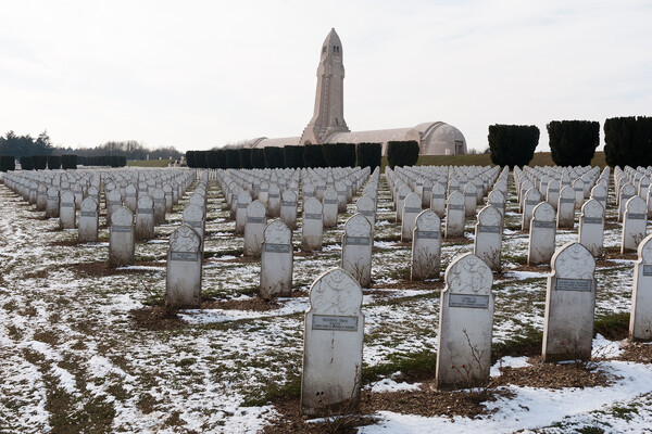 A snowy field of marked gravestones, with yew hedges and a large obelisk in the background