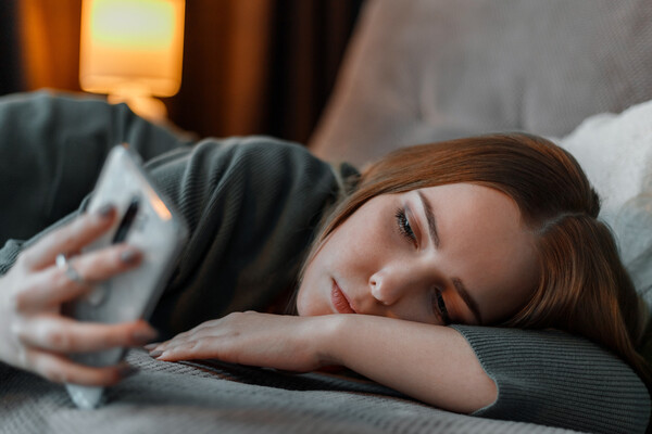 A young woman lies sideways on a bed, gazing at her phone