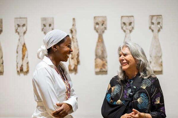 two artists laughing with each other standing in gallery in front of wooden balusters on wall