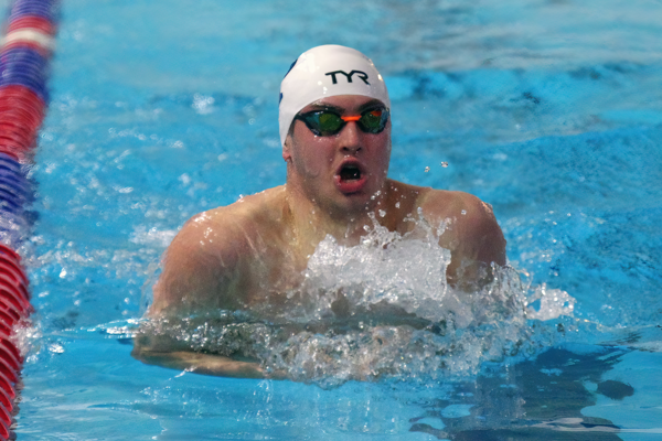 Wearing a white swim cap and goggles, Matt Fallon performs the breaststroke during a meet.
