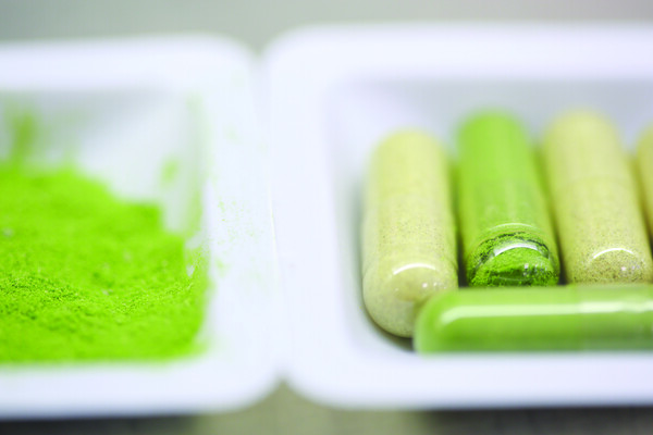 Two trays, one with four filled capsules, the other with green powder that will fill empty capsule shells.