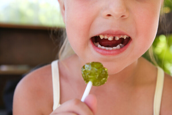 A child with damaged teeth eating a lollipop.