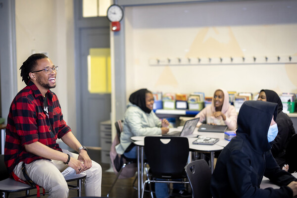 tamir harper sitting on a desk laughing with students