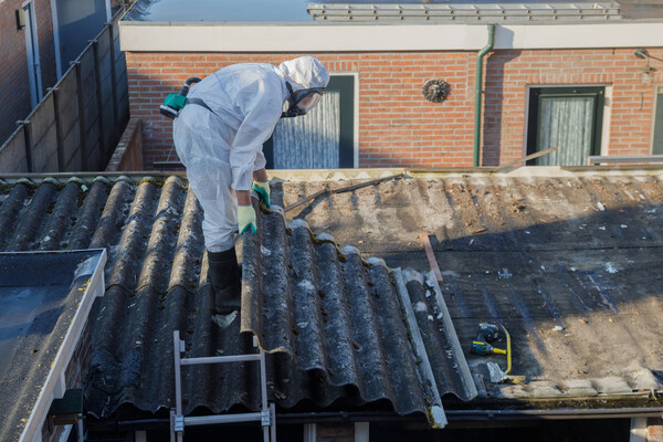 A person in a hazmat suit removes a piece of roofing from a roof.