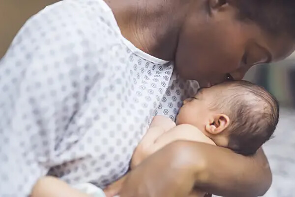 African American person kisses the head of their newborn baby.