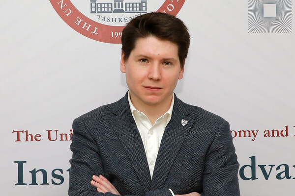Political Science Ph.D. candidate Mikhail Strokan stands in front of a sign with a seal that reads "Tashkent."