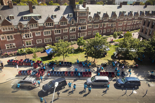 overhead shot of cars parked next to sidewalk filled with moving carts outside of The Quad College House