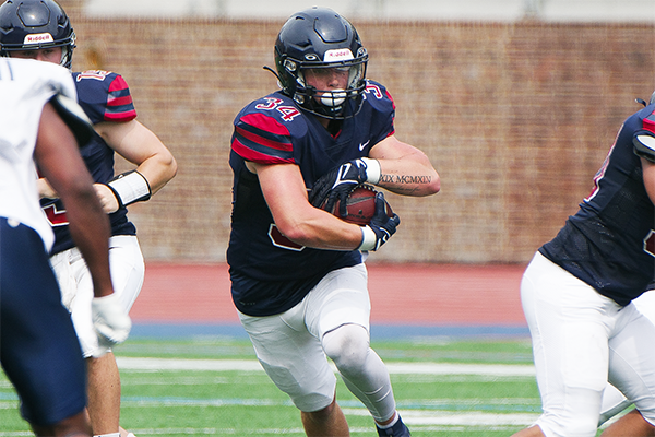 JT Goodman, a running back on the sprint football team, carries the ball through a large hole created by two blockers.