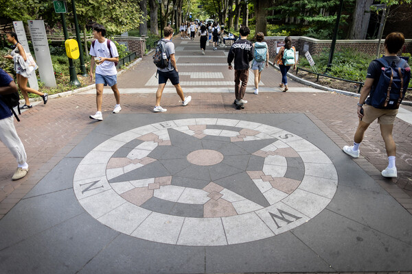 Students walk around a compass embedded in Locust Walk on Penn campus.
