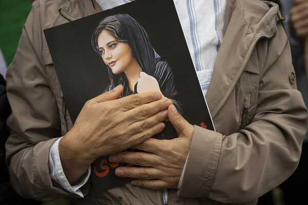 A person is shown holding a photo of Mahsa Amini, a woman who was killed in police custody in Iran in 2022.