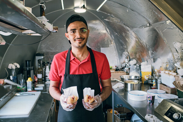A fast food kitchen employee holding two hot dogs.