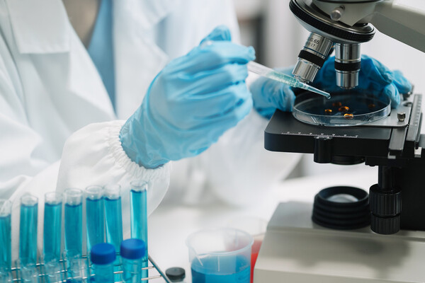 A person wearing latex gloves using a pipette and a microscope in a lab.