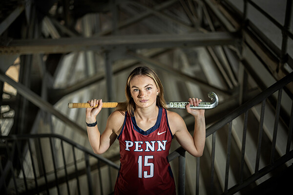 Allison Kuzyk, wearing her Penn uniform, holds her field hockey stick across her shoulders on steps inside Franklin Field.