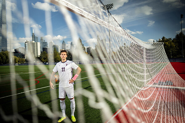 Stas Korzeniowski stands inside a goal at Penn Park with the Philly skyline in the background.