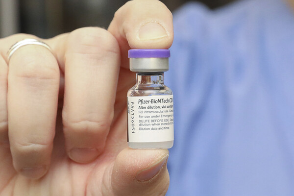 Hand holding a vial of Pfizer vaccine.