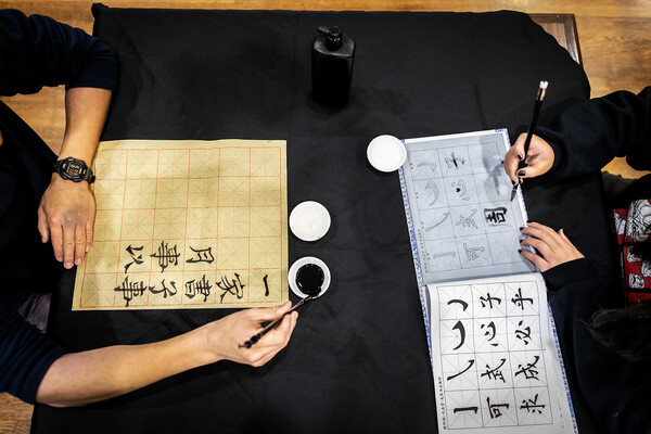 Hands holding calligraphy brush as they paint. 