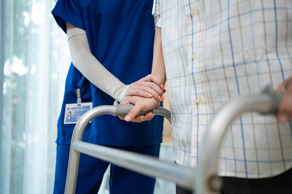 A health professional assists a person with a walker.
