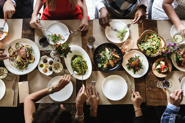 Overhead image of a table set with food and diners hands and arms cutting food and and eating.