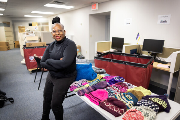 Isabel Sampson-Mapp sits on a table piled with colorful knitwear