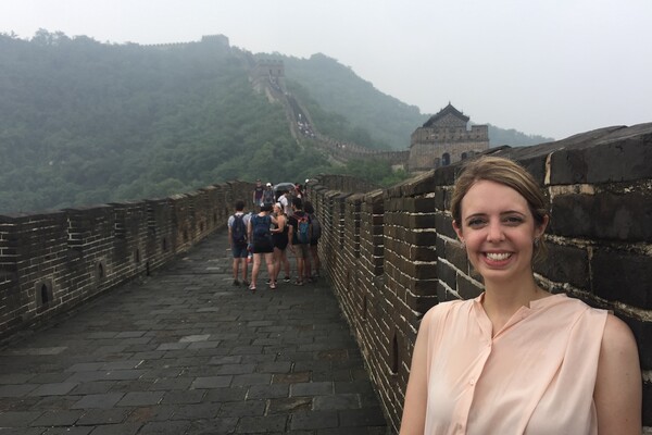 Rachel Hulvey stands on the Great Wall of China, with a hazy mountain in the background.