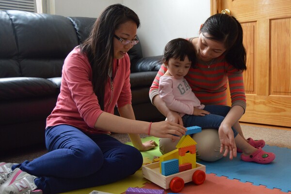 Two women help a child balance building blocks