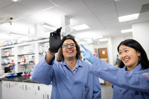 Researchers Mike Mitchell and Emily Han examining a microfluidic device used to make LNPs by mixing lipids and mRNA.