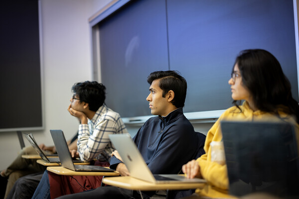 Three students gaze at the front of the class, laptops open 