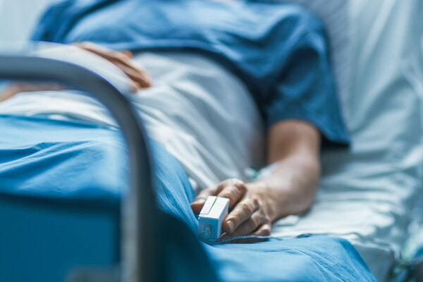 A patient in a hospital bed with an oxygen reader on their finger.