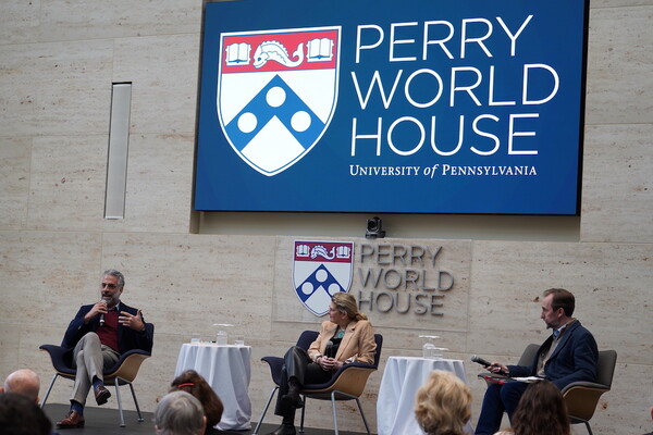 Three people sit on a stage in front of a screen reading Perry World House, University of Pennsylvania.