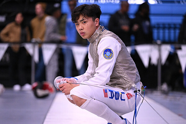 Bryce Louie kneels down with his fencing foil sword.