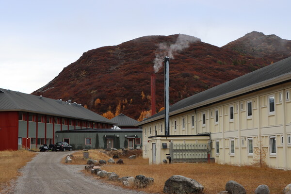 Two long, two-story buildings located off of a gravel road. Two smokestacks are in the foreground. 