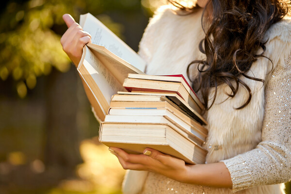 A person holding a stack of books while reading one.