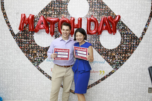 Two Penn Med students hold Match Day signs in front of Match Day balloons at Penn Medicine.