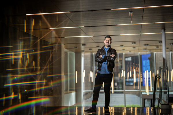 Andres Oliveros Gonzalez posing with crossed arms in GSE building with lights reflecting off to the side. 