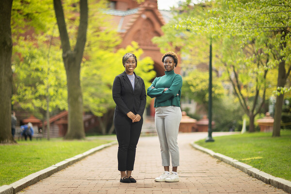 Taussia Boadi and Cheryl Nnadi pose on Penn's campus in front of College Hall, green grass and a huge tree.