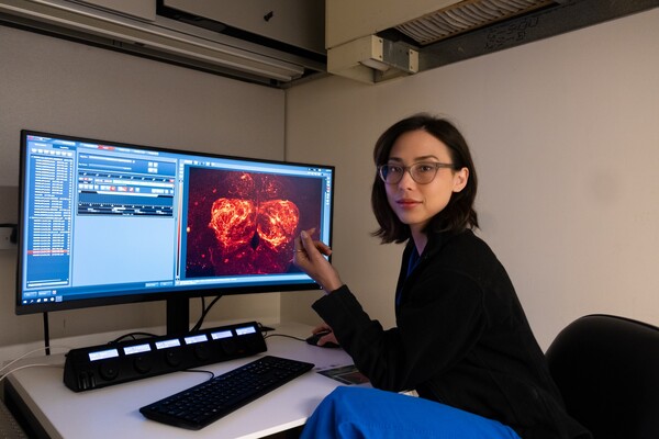 Photograph of researcher, China Byrns, in front of monitor showing microscopy images of fly brain