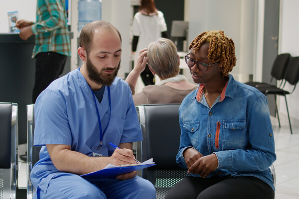 A medical professional and a patient in a waiting room filling out a form.