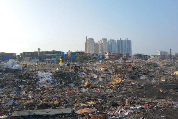 An image of people picking through a dump with a handful of skyscrapers along the horizon